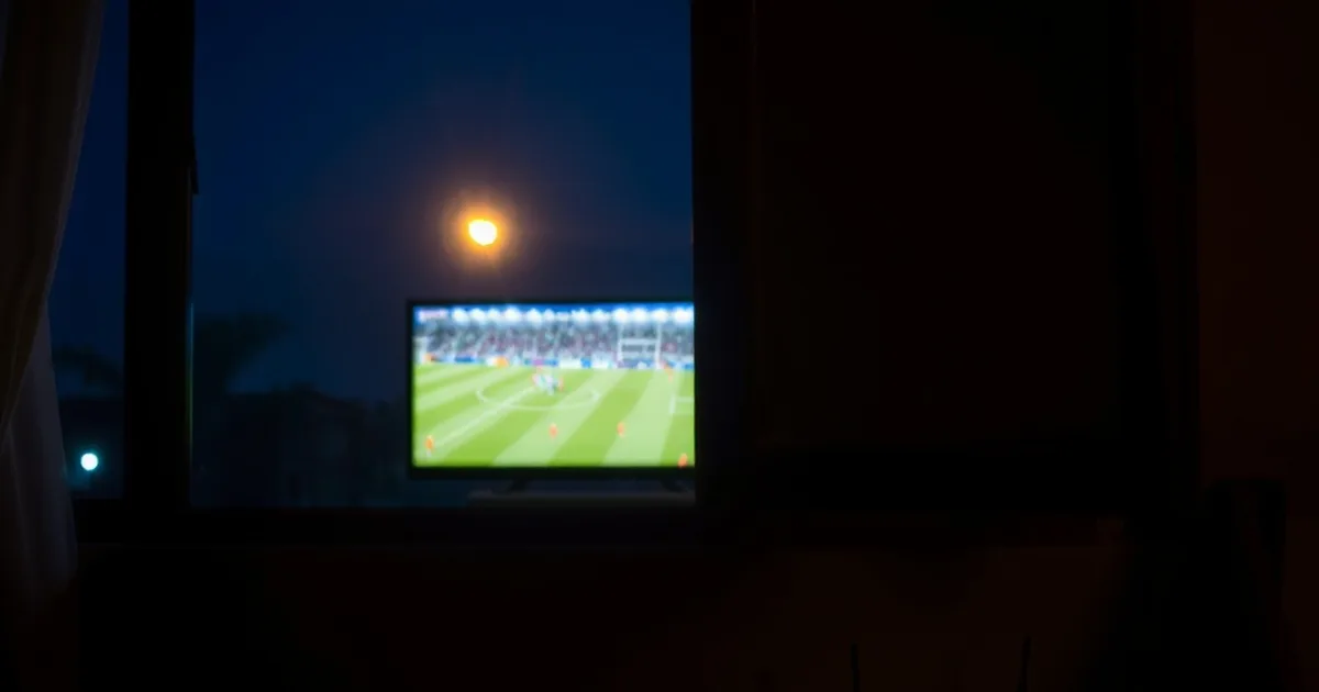 Salon faiblement éclairé la nuit avec une télévision diffusant un match de football et un routeur 4G visible à proximité, ambiance loin de la ville